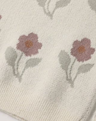Close-up of an ivory knit sweater's floral pattern, showing dusty pink flowers with orange centers and sage green leaves.