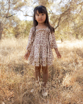 Little girl standing in golden field wearing ivory floral toile dress with balloon sleeves