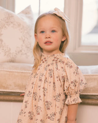 Close-up of toddler girl in blush floral smocked dress with puff sleeves and matching bow