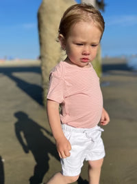 Child wearing a red striped shirt and white shorts standing outdoors on a sunny day.