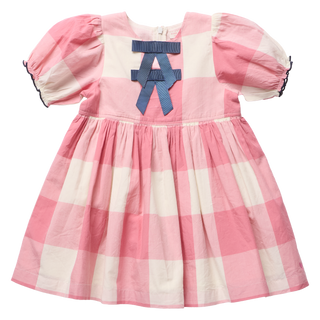 Front view of a pink and cream check dress with puff sleeves, navy ruffle trim, and a navy grosgrain bow detail at the neckline, on a white background.