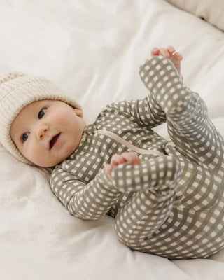 Baby wearing a checkered onesie and cream hat on a white blanket