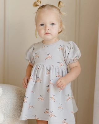 Young girl wearing a light blue dress with deer pattern against a neutral background