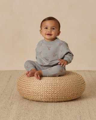 Baby sitting on a woven stool against a beige background