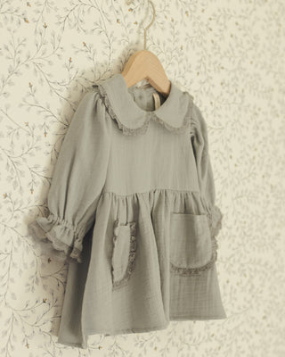 Vintage-style blue gray dress with ruffled collar and cuffs on a floral wallpaper background