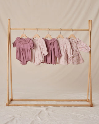 Wooden clothing rack with baby clothes on a beige background