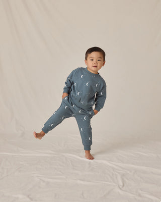 Child wearing a blue pajama set with moon patterns on a beige background