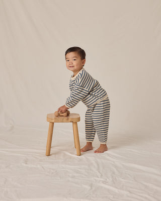Child in striped pajamas standing on a small wooden stool against a plain background