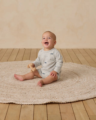 Baby sitting on a textured rug with a wooden floor and beige wall in the background