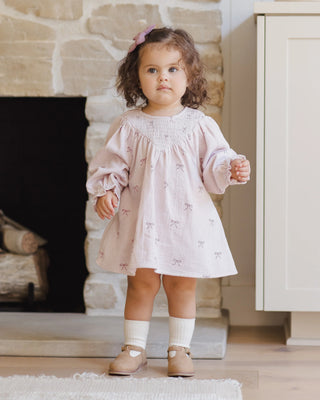 Young child wearing a light pink dress with a fireplace in the background