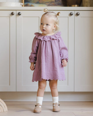 Young child wearing a purple dress standing in a kitchen.