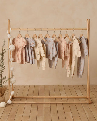 Wooden clothing rack with baby clothes on a wooden floor against a beige wall.