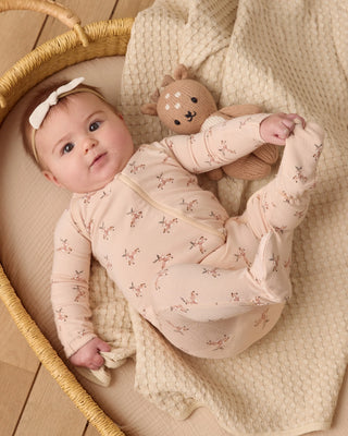 Baby in a pink floral outfit lying on a textured blanket with a teddy bear.