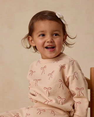 Child wearing a pink outfit with bow patterns on a beige background