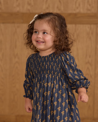 Child wearing a blue dress with a floral pattern against a wooden background