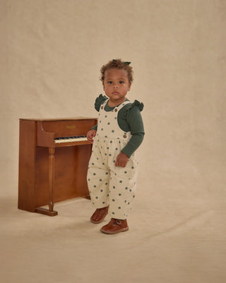 Child in a polka dot outfit standing next to a wooden piano on a beige background