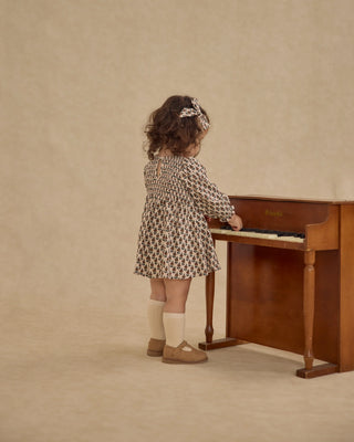 Young girl playing a wooden piano against a beige wall