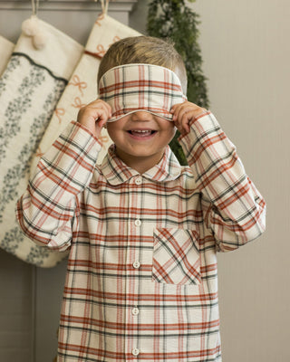 Child wearing a plaid shirt and headband, standing in front of Christmas stockings.