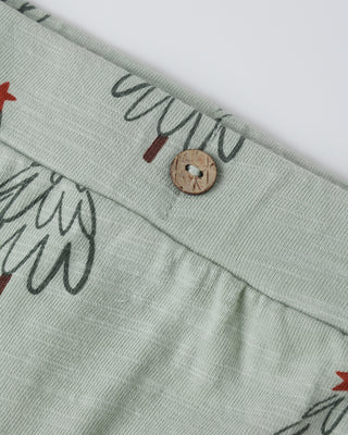 Close-up of a light green fabric with leaf patterns and a wooden button on a white background