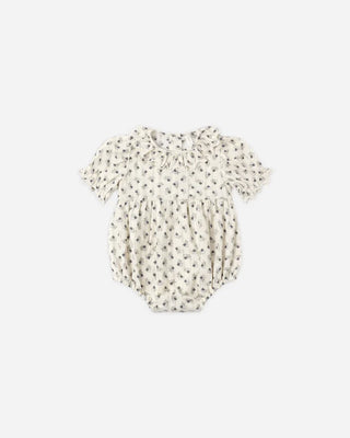 Front view of a natural cream floral print bubble romper laid flat, featuring a ruffled collar, short puff sleeves with ruffled cuffs, a gathered waist, and bloomer-style bottom.