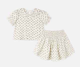 Ivory floral print top and skirt set laid flat, featuring a ruffled collar and puff sleeves on the top, paired with a smocked-waist skirt with a scalloped hem, both in a small grey floral pattern.