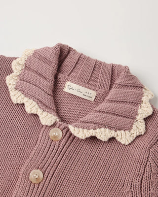 Close-up of a rosewood pink knit cardigan's scalloped collar with cream crochet trim and mother-of-pearl buttons, showing the interior brand label.