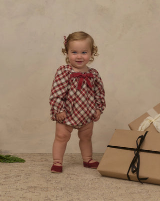 Baby wearing the Noralee Annette Romper in red Holiday Tartan with long puff sleeves, standing beside wrapped gifts
